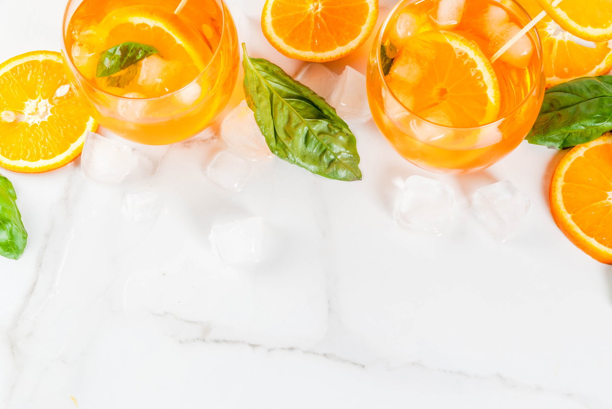 Gläser mit Orangenlimonade und Basilikum zwischen Eiswürfeln.