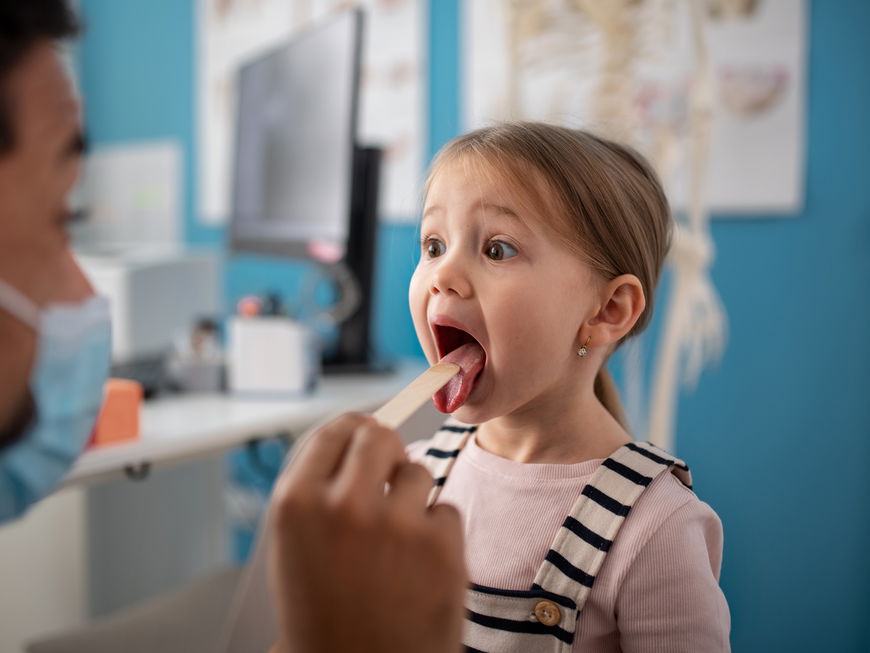 Kinderarzt schaut einem Mädchen in den Rachen.