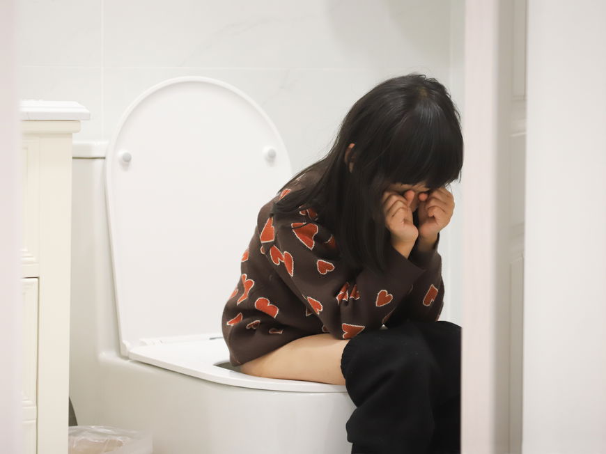 Verstopfung bei Kindern Lösen: Kind sitzt mit Verstopfung auf Toilette.