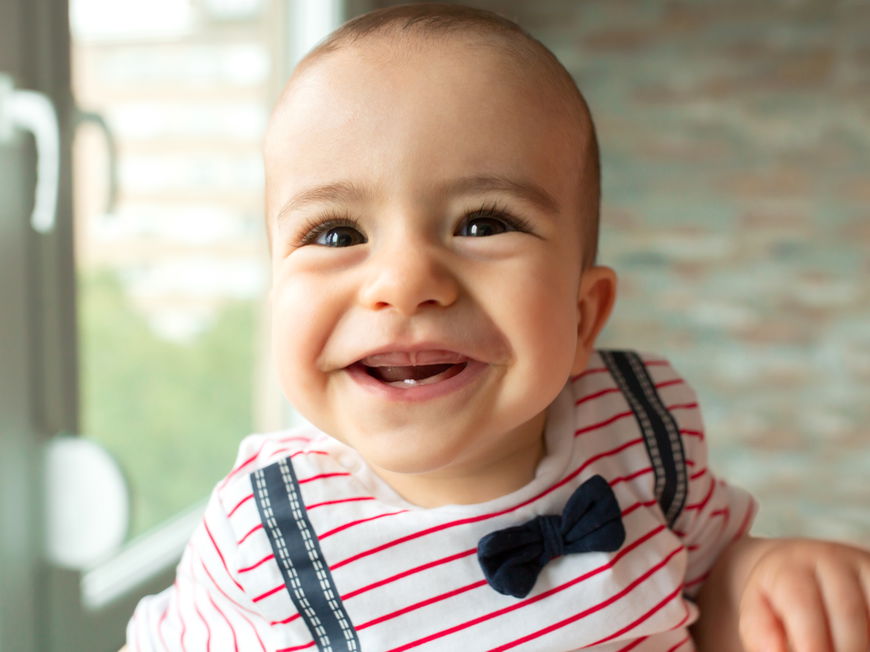 Baby mit frischem Zahn lacht in die Kamera.
