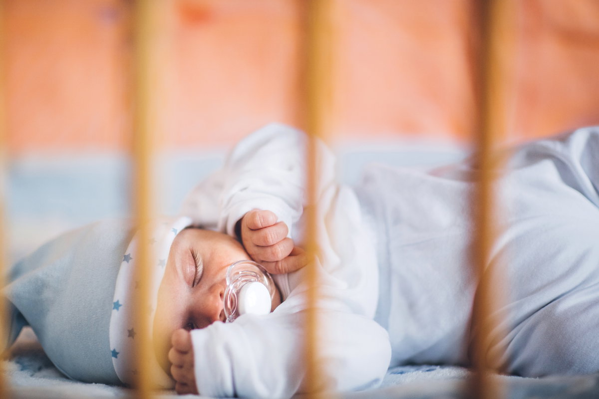 Ein Baby schläft in einem Bettchen mit einem Schnuller.