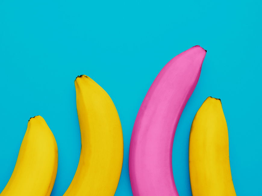Eine lange pinke Banane neben drei kleineren gelben Bananen als Symbol für unterschiedliche Penislängen