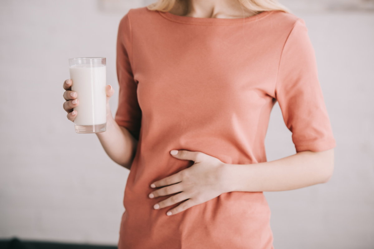 Frau hält ein Glas Milch in der Hand und hat Bauchschmerzen