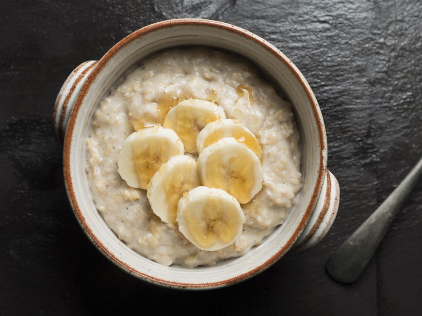 Draufsicht einer Schüssel Porridge mit Bananenscheiben und Honig