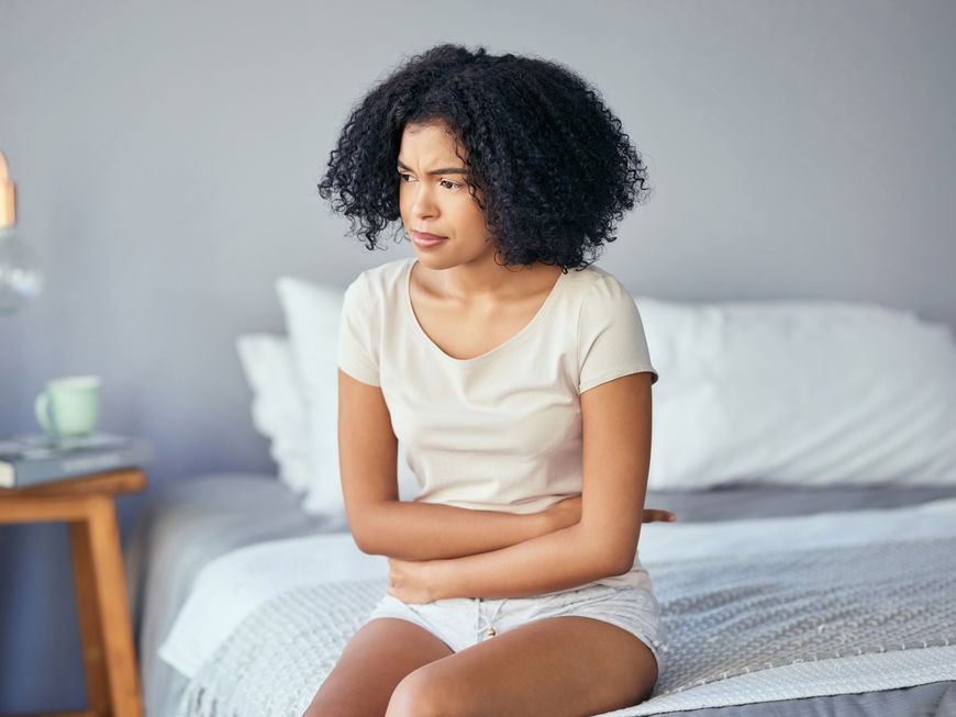 Frau mit Unterleibschmerzen sitzt im Bett