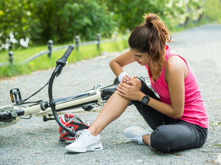 Junge Frau hatte einen Unfall mit dem Fahrrad und hält sich das Knie.
