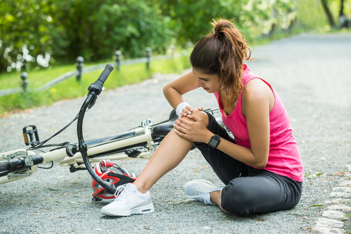 Junge Frau hatte einen Unfall mit dem Fahrrad und hält sich das Knie.