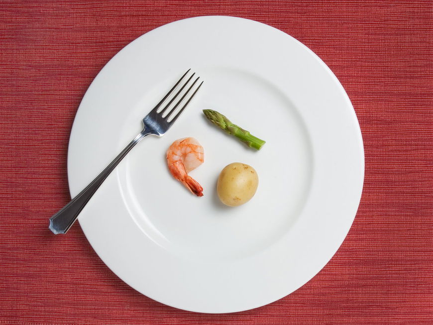 Großer Teller mit einer kleinen Kartoffel, einem Shrimp und einem Stück grünem Spargel darauf