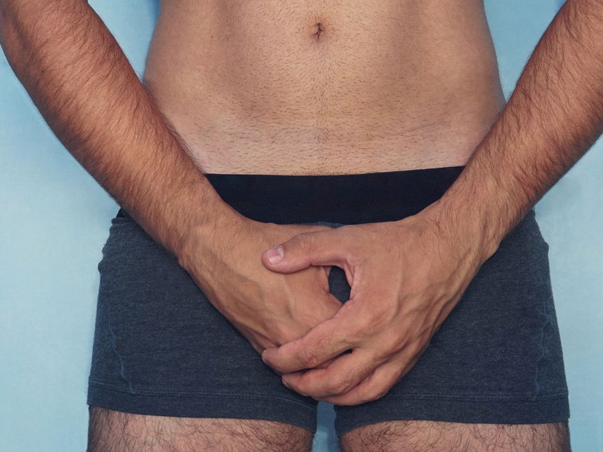 Mann hält sich die Hände schützend vor den Intimbereich