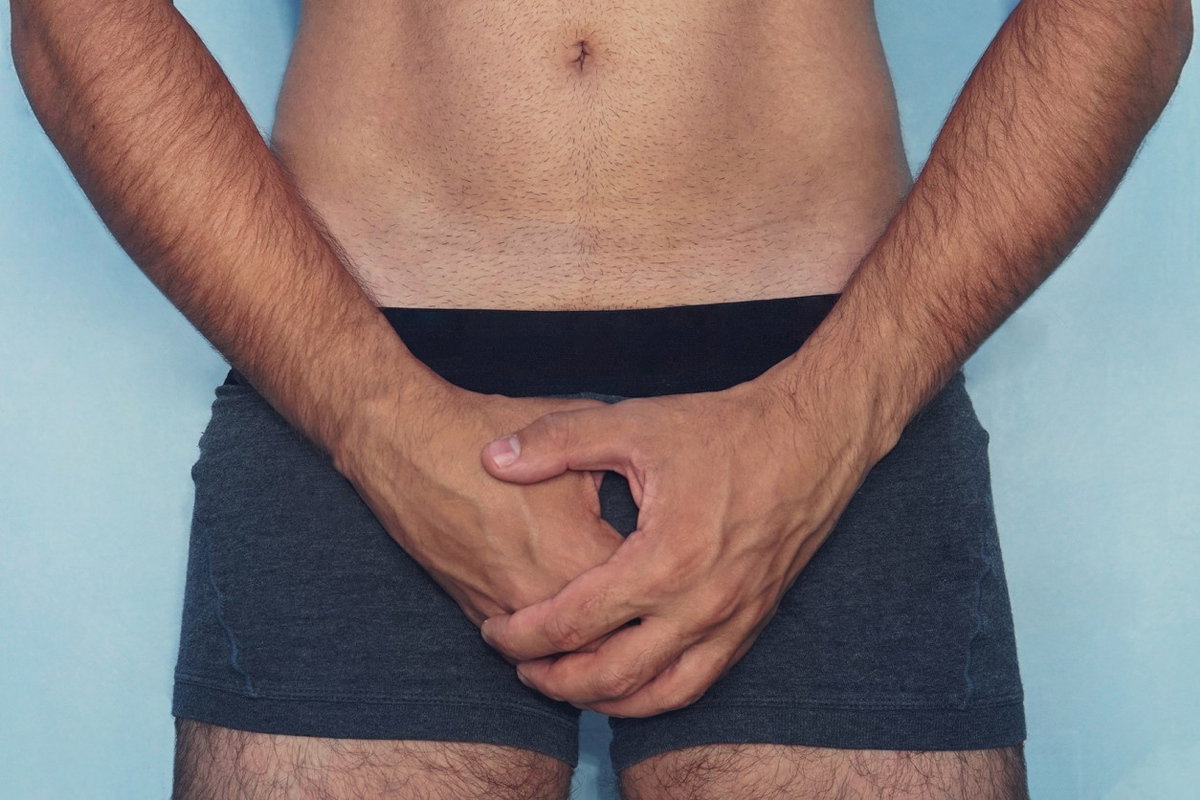 Mann hält sich die Hände schützend vor den Intimbereich