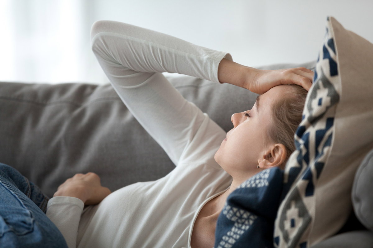 Frau liegt mit Migräne auf dem Sofa