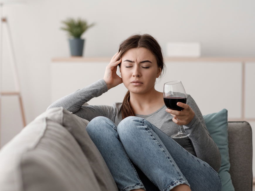 Frau sitzt mit einem Glas Wein in der Hand auf dem Sofa und fühlt sich unwohl