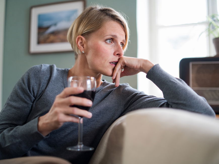 Nachdenkliche Frau sitzt auf dem Sofa mit einem Glas Wein in der Hand
