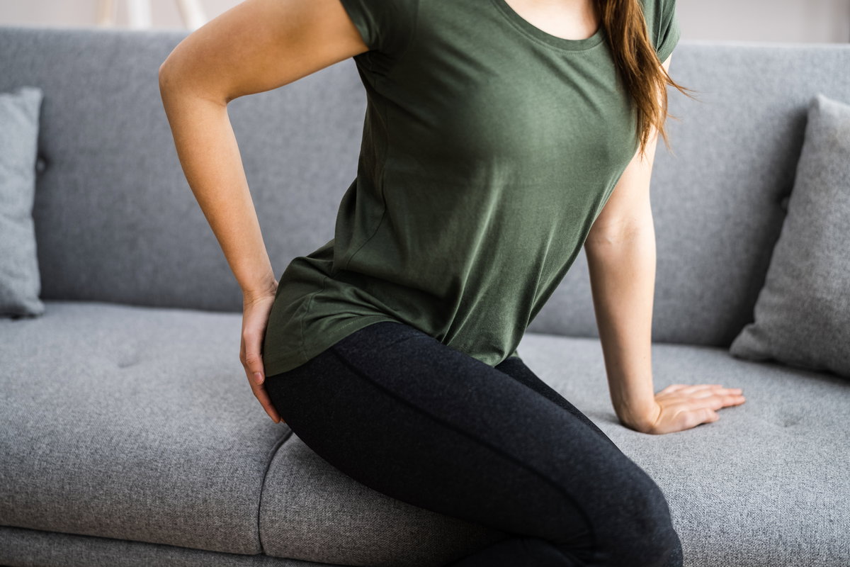 Frau sitzt auf Sofa und fasst sich ans Gesäß