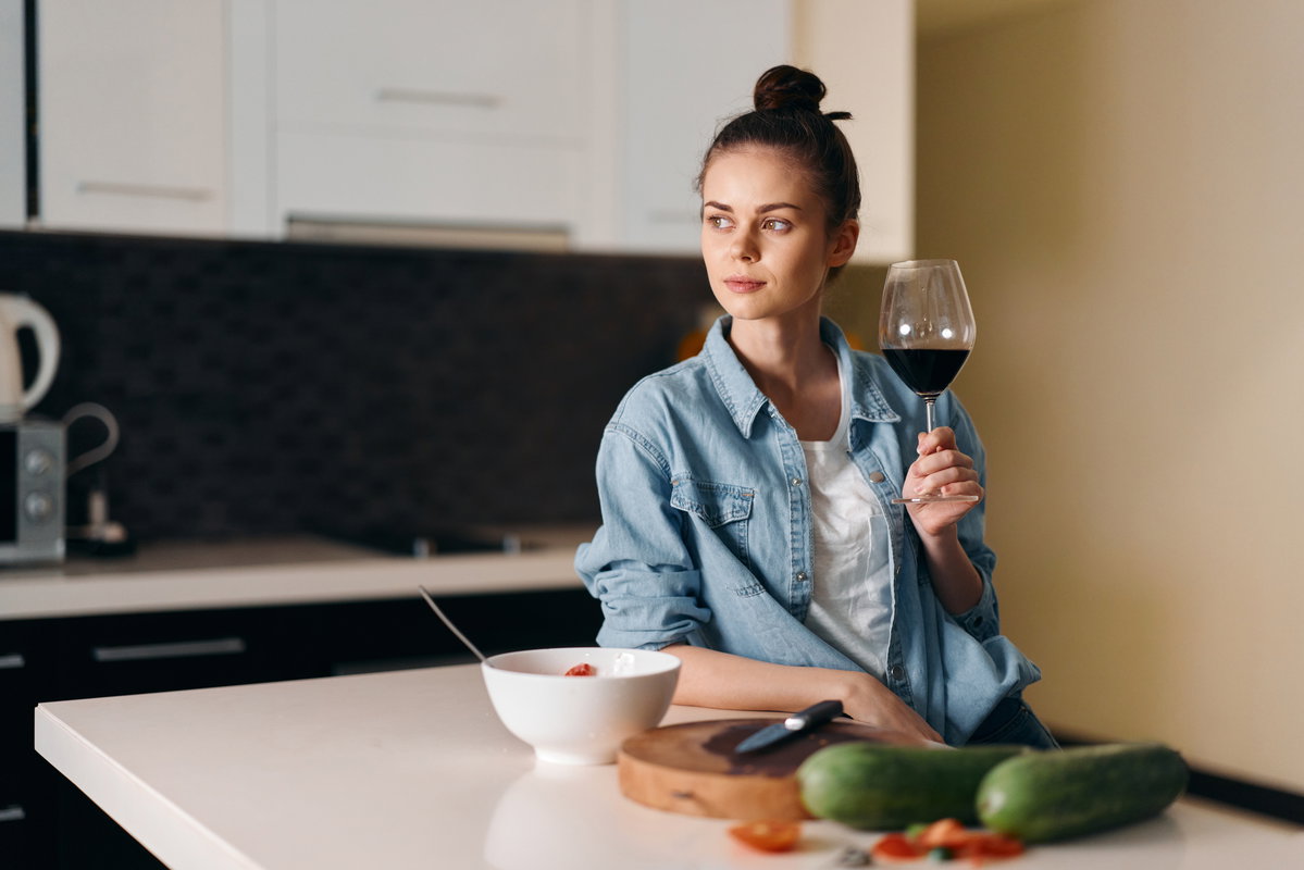 Frau steht in der Küche und trinkt Wein
