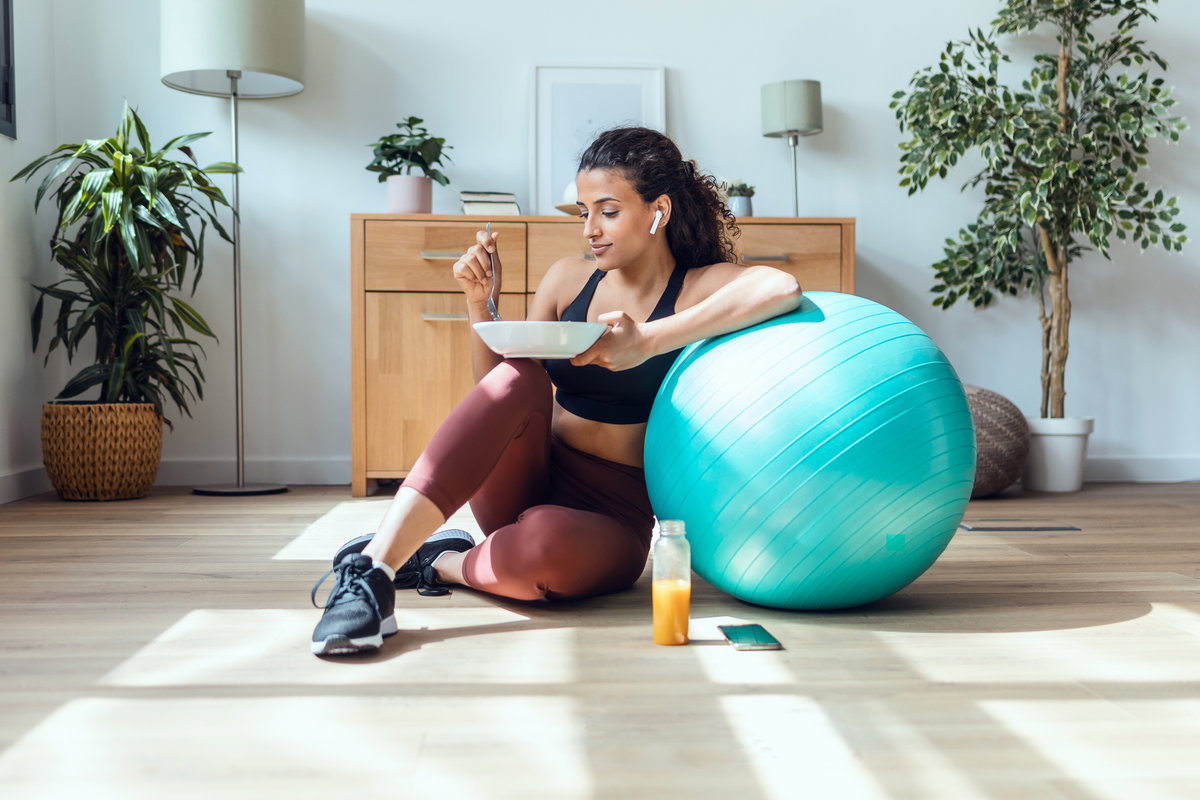 Frau sitzt neben Gymnastikball mit gesundem Essen
