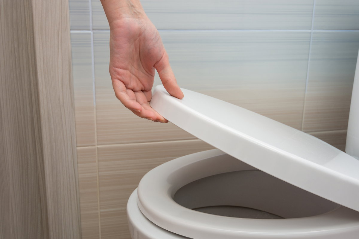 Hand, die Toilettendecke hochhebt