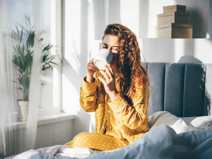 Frau trinkt im Bett eine Tasse Kaffee