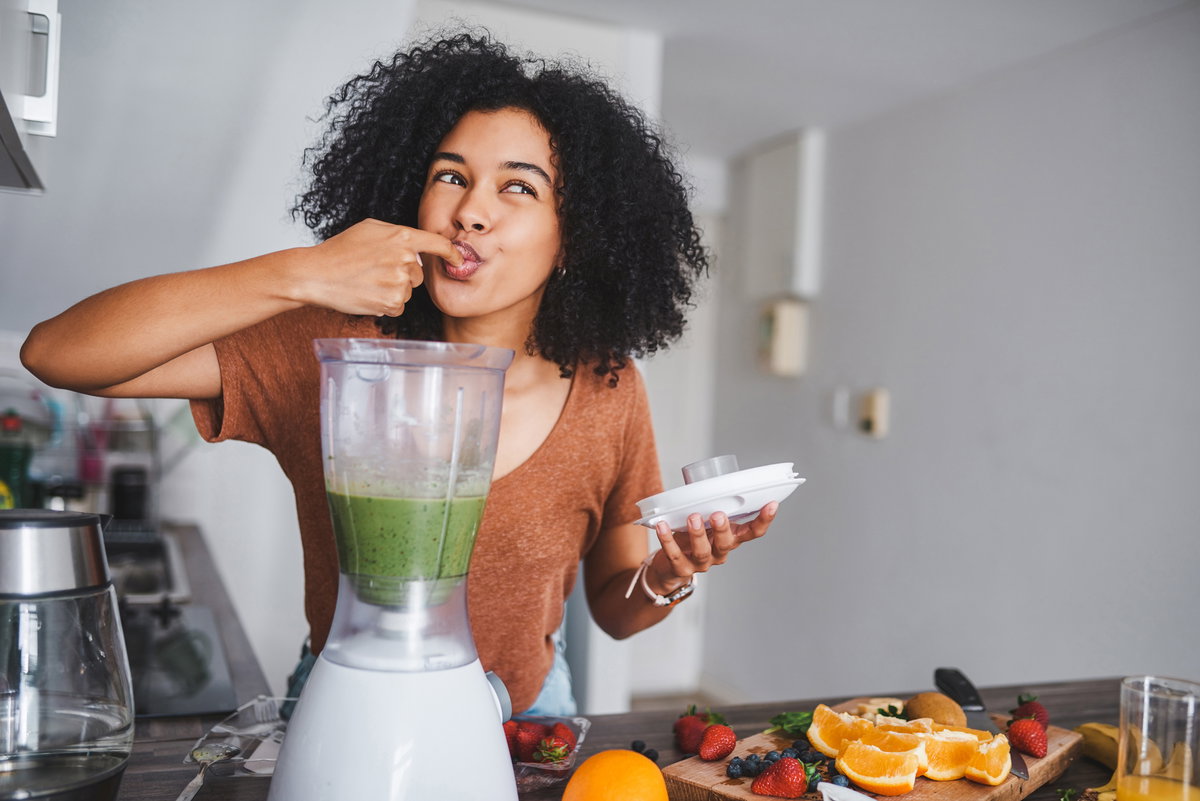 Frau steht vor dem Mixer und probiert grünen Smoothie