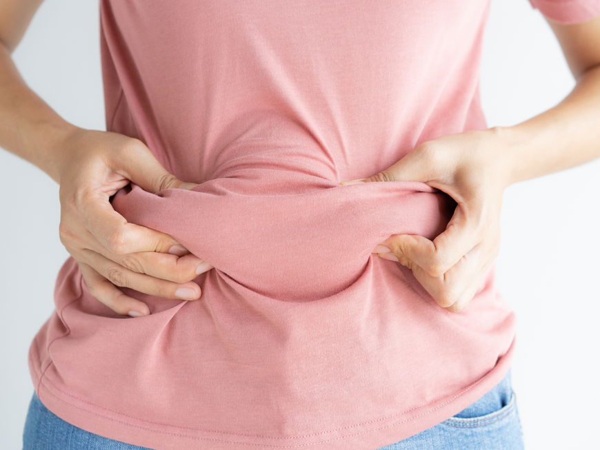 Frau fasst das Fett am Bauch unter ihrem T-Shirt an