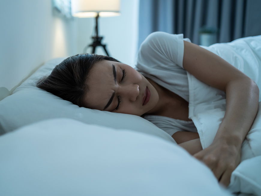 Frau liegt im Bett und träumt schlecht