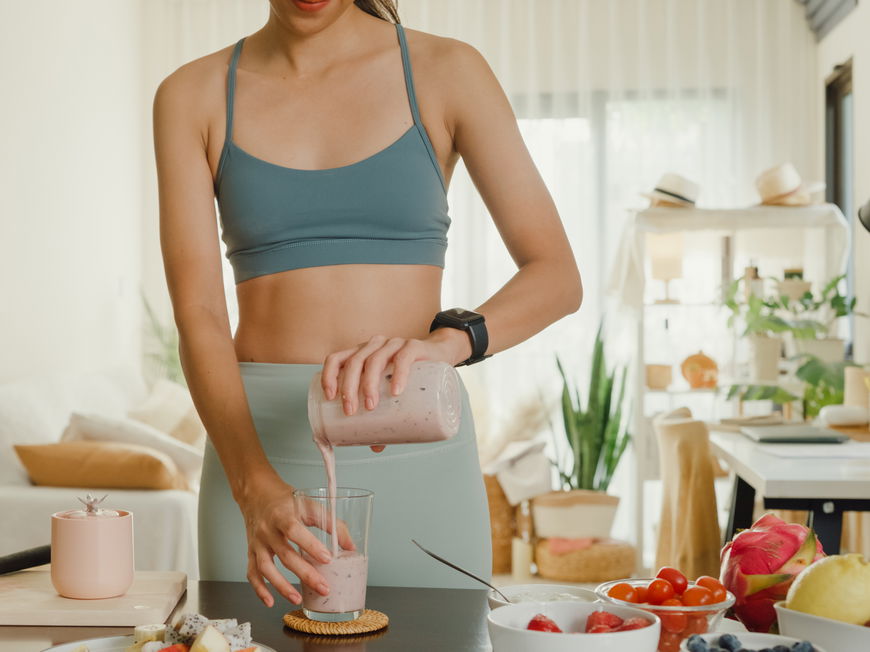 Frau im Sportoutfit macht sich Proteinshake