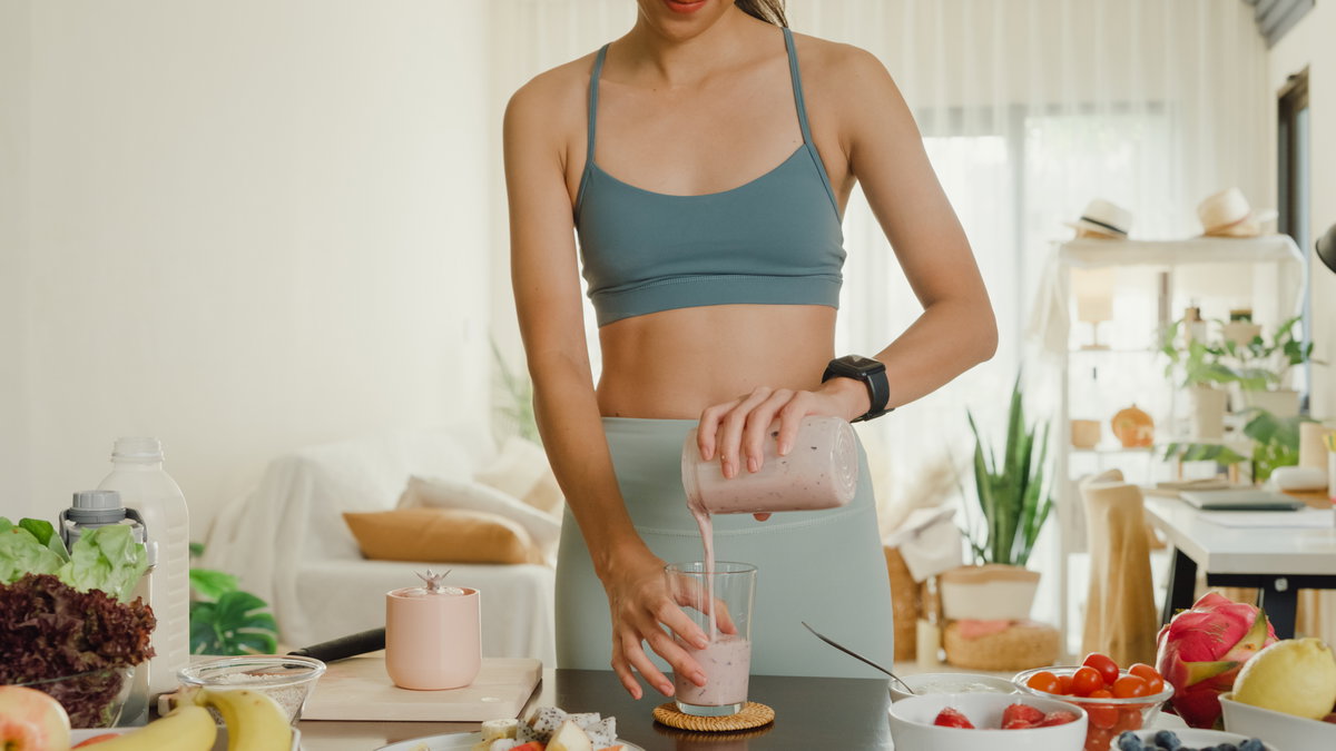 Frau im Sportoutfit macht sich Proteinshake