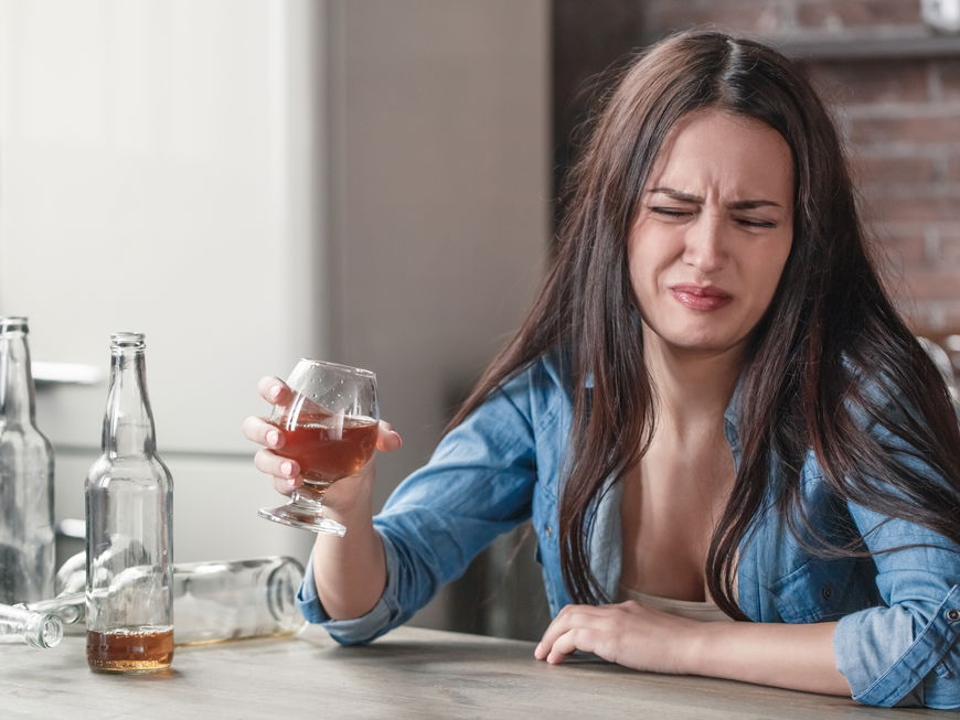Frau verzieht das Gesicht und hält ein Glas in der Hand