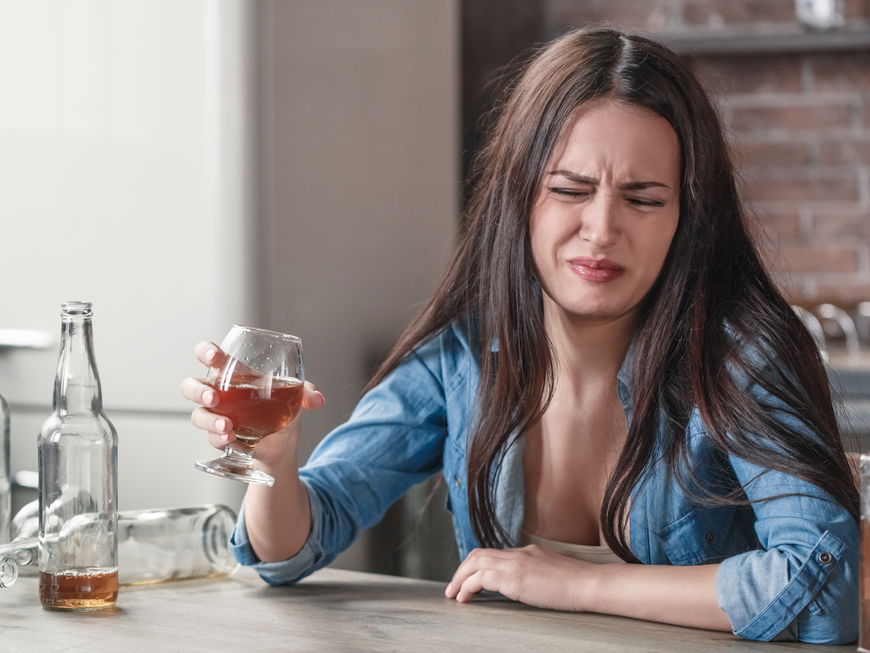 Frau verzieht das Gesicht und hält ein Glas in der Hand
