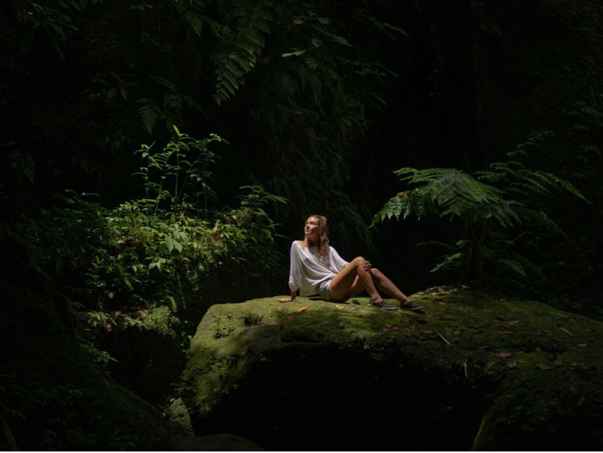 Eine Frau sitzt auf einem Felsen im Regenwald