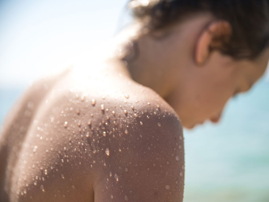 Eine Junge Frau, die sich im Sommer am Wasser befindet und deren Rücken mit Wasserperlen überzogen ist