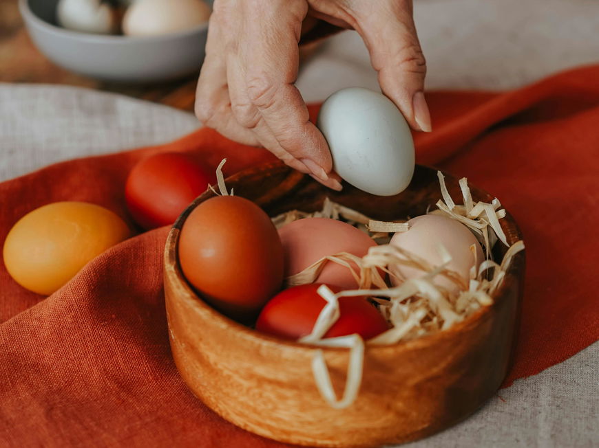 Eine Schale mit bunt gefärbten Bio-Ostereiern auf einem Nest aus Heu