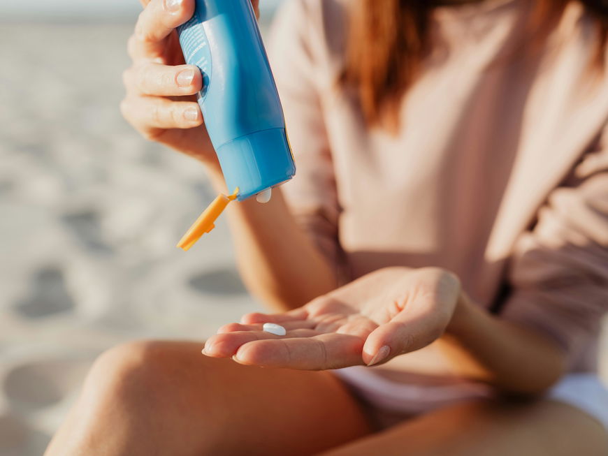 Frau cremt sich am Strand mit Sonnencreme ein
