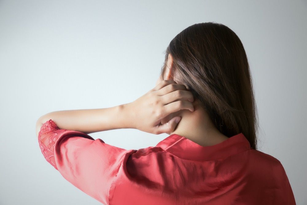 Frau juckt sich mit der Hand am Nacken.