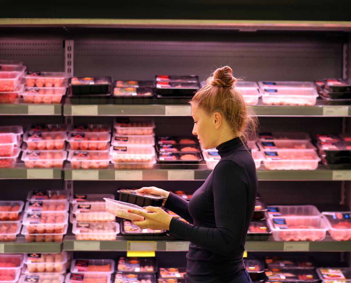 Frau im Supermarkt vor Fleischregal