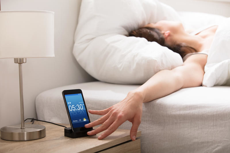 Frau im Bett drückt Snooze Taste Wecker