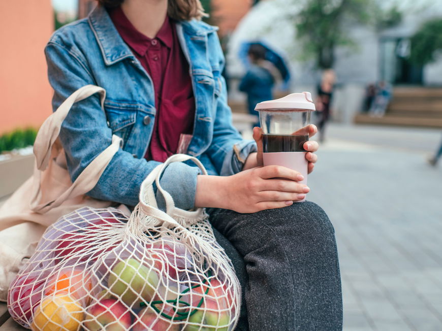 Frau mit nachhaltigen Alternativen mit Obstnetz und Kaffeebecher