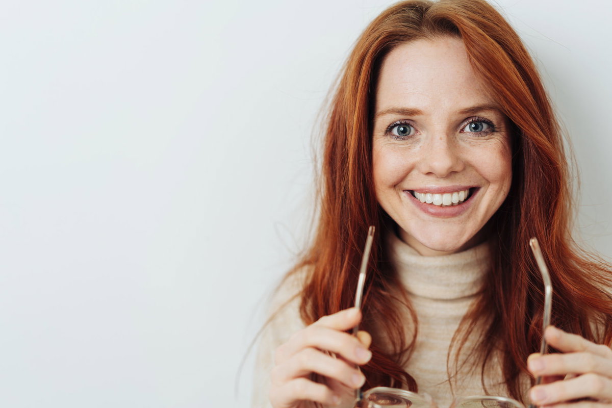Frau mit strahlenden Augen und Brille in der Hand