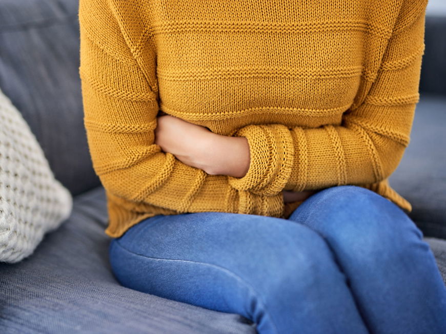 Frau sitzt auf Sofa und hält sich den Bauch